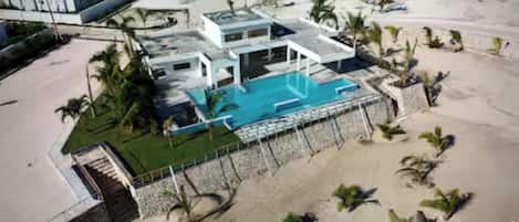 A modern hotel with a pool, surrounded by palm trees and a beach.