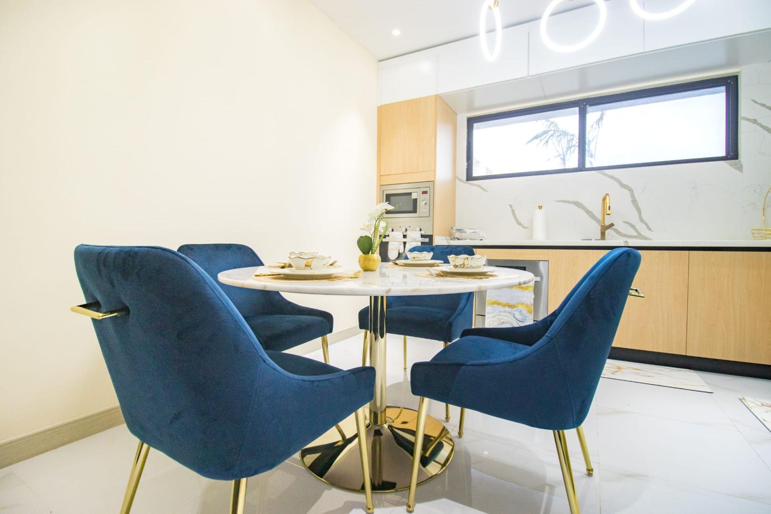 A modern kitchen with a round dining table and blue chairs, a window, and a built-in oven.