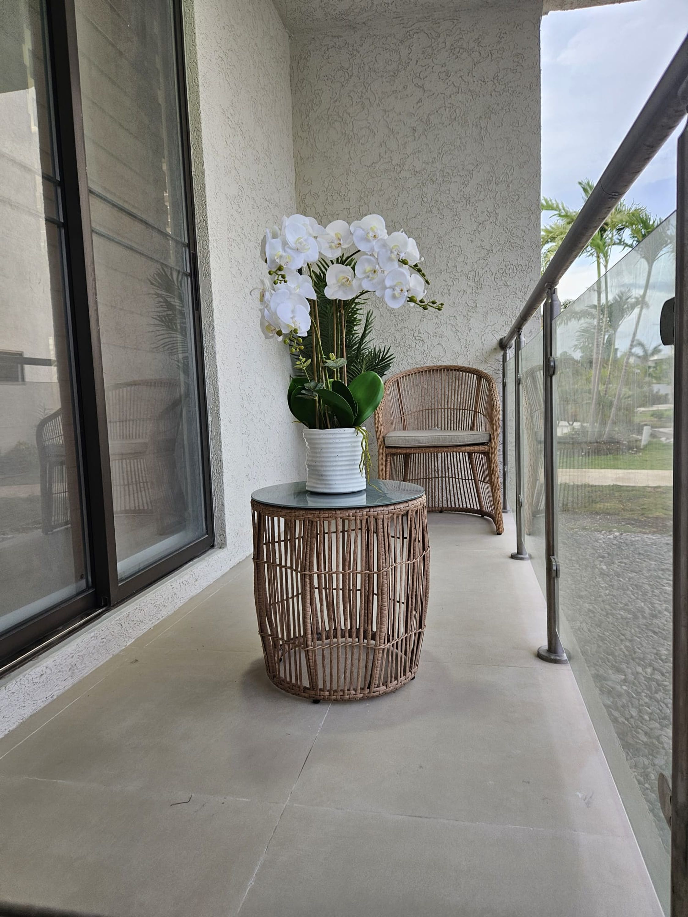 A balcony with a wicker round table, a potted orchid, and a wicker chair.