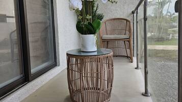 Uma varanda com uma mesa redonda de vime, uma orquídea em vaso e uma cadeira de vime.