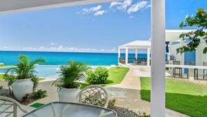 Un espacio exterior techado con vista al océano, una piscina y un edificio blanco con una puerta azul.