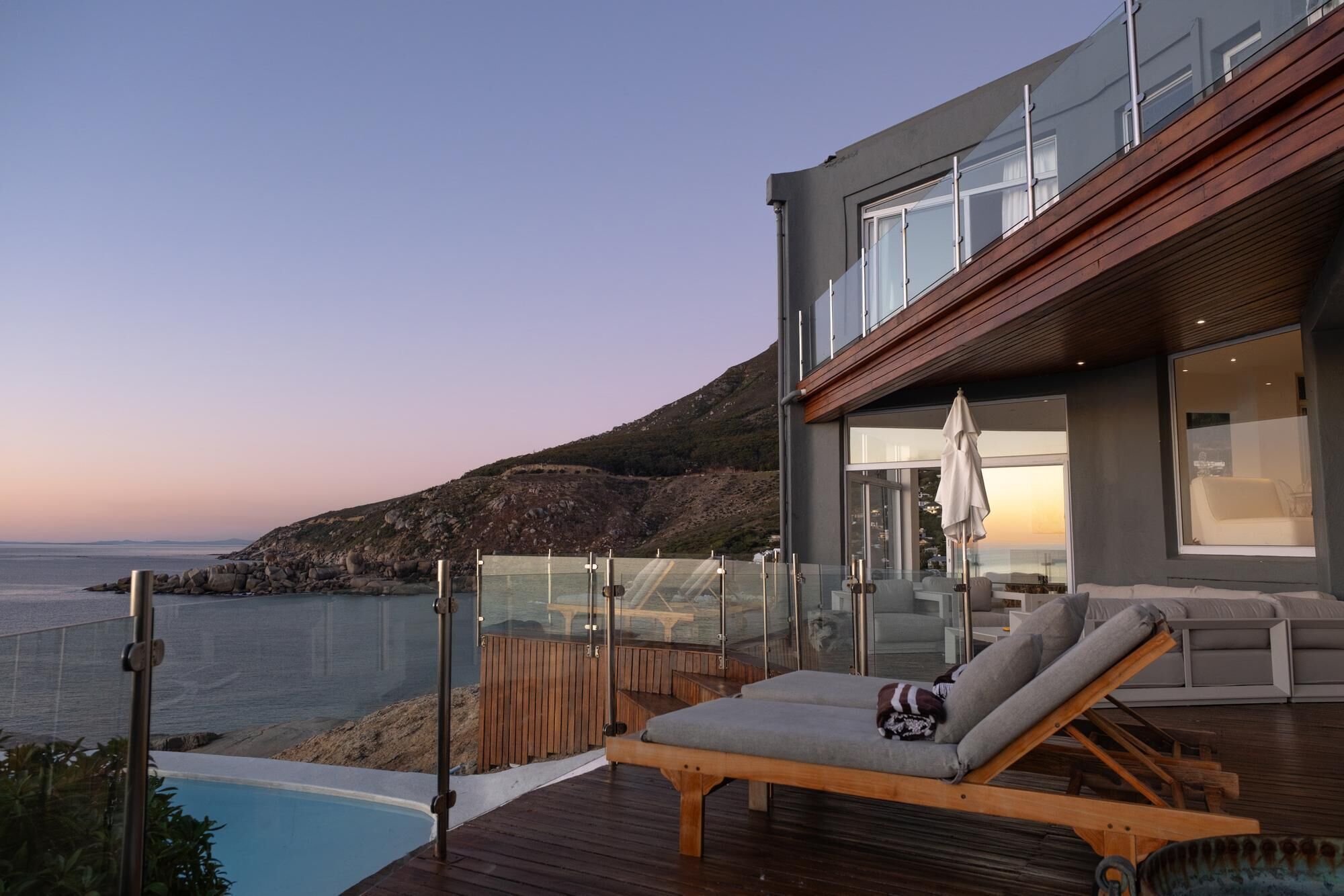 Ein modernes Haus mit Pool, Liegestühlen und Meerblick.