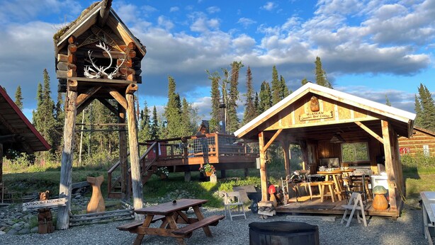 A rustic wooden cabin with a bear sculpture, an outdoor kitchen, and a dining area.