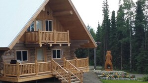 A log cabin with a balcony, a fireplace, and a bear statue in the yard.