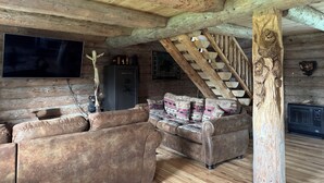 A rustic cabin interior with a wooden ceiling, a sofa set, a television, and a staircase.