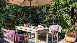 Eine Terrasse im Freien mit Tisch, Stühlen, einer Bank, einem Sonnenschirm und einem Blumentopf.