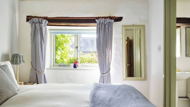 Een slaapkamer met een bed, een raam met gordijnen, een bedlamp en uitzicht op groen.