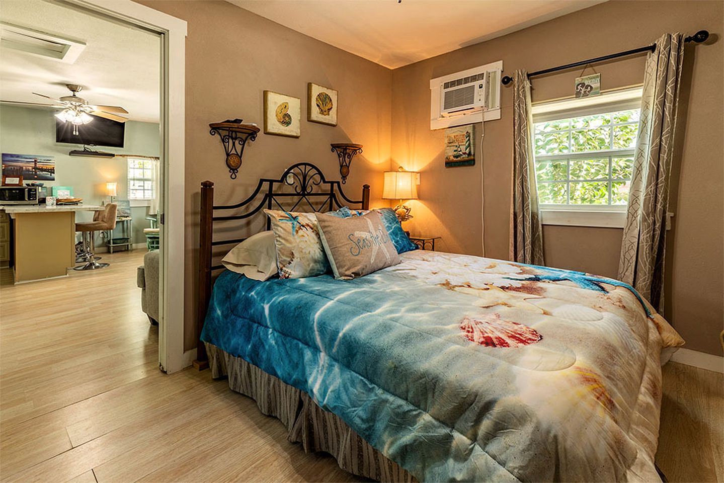 A bedroom with a bed, bedside lamps, a window with curtains, a ceiling fan, and artwork on the wall.