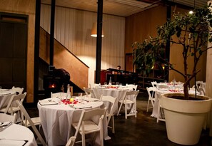 Un restaurant avec des tables rondes, des chaises blanches, un piano et une grande plante en pot.