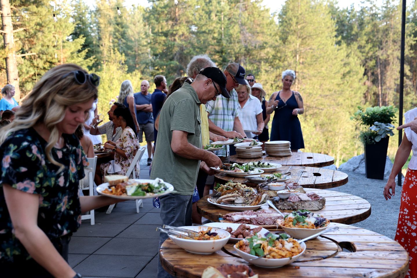 An outdoor dining area with multiple round tables, guests seated, and food being served.