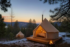 Een tent met een bed aan de binnenkant, omgeven door bomen en uitzicht op een berg.