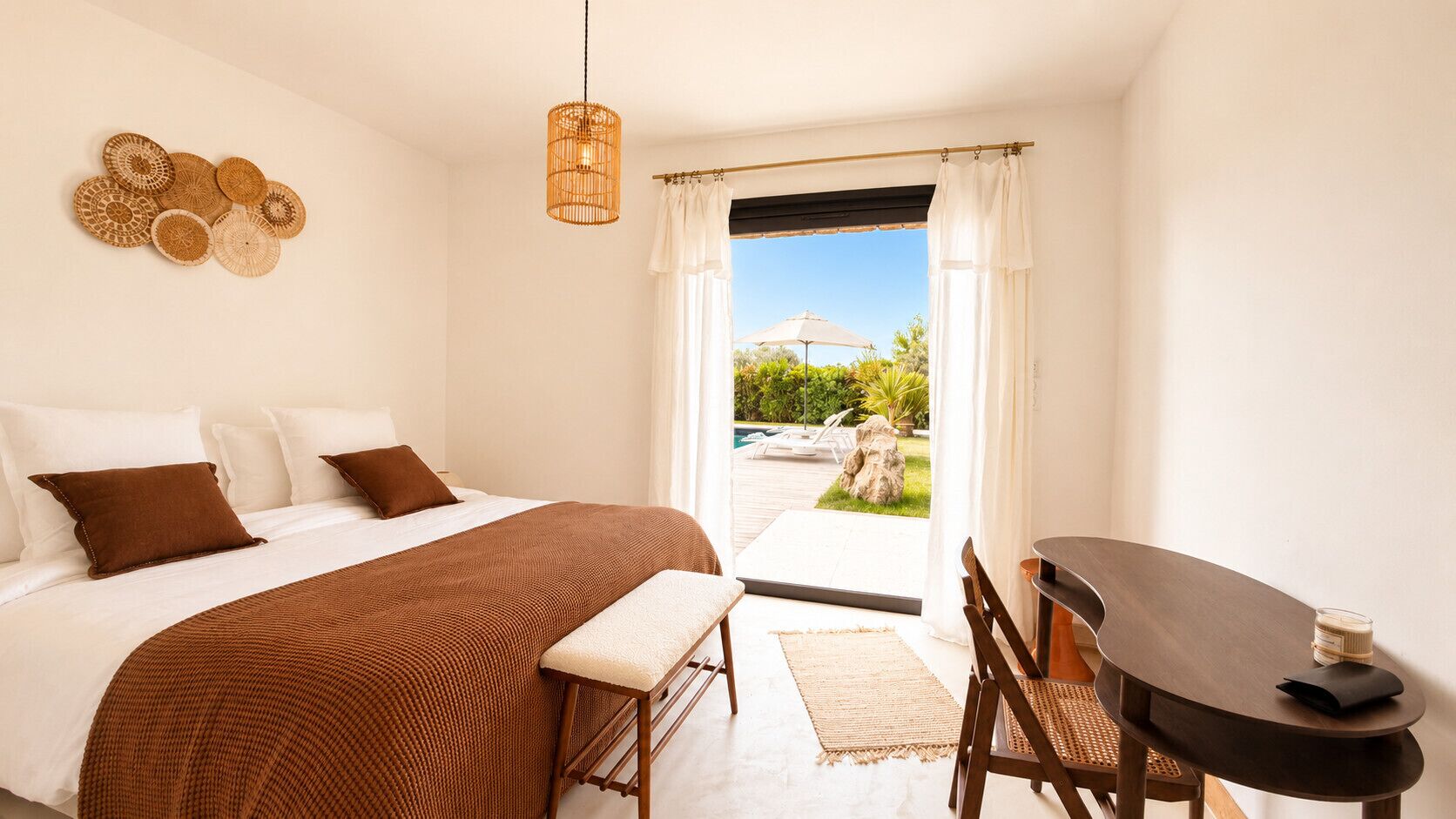 A bedroom with a bed, bedside table, bench, and a view of an outdoor area.