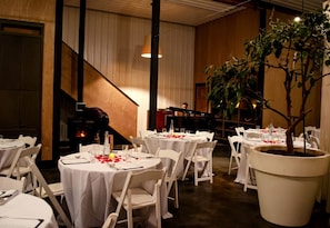 Ein Restaurant mit runden Tischen, weißen Stühlen, einem Klavier und einer großen Topfpflanze.
