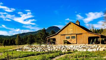 A wooden barn with a covered porch, surrounded by a stone wall and a grassy field.