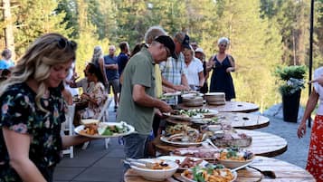Un área de comedor al aire libre con mesas redondas, comensales sentados y comida siendo servida.
