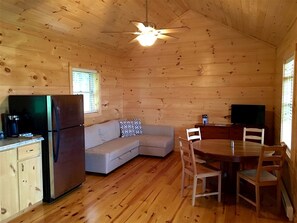 Interior de una cabaña con cocina, un sofá, una mesa de comedor y un ventilador de techo.