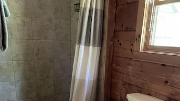 A bathroom with a shower, toilet, and a window.