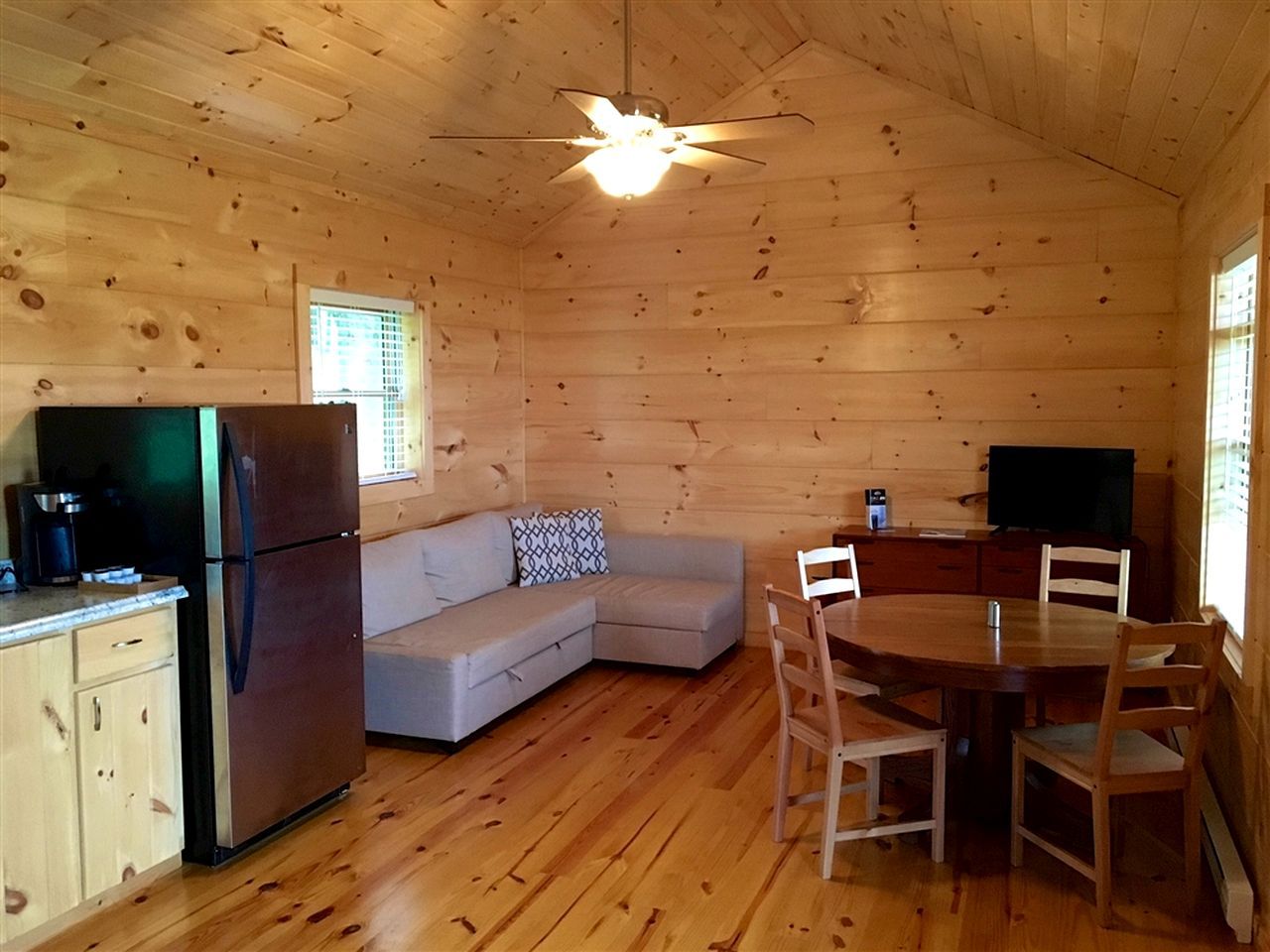 A cabin interior with a kitchen, a sofa, a dining table, and a ceiling fan.