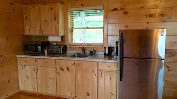 A compact kitchen with wooden cabinets, a stainless steel refrigerator, a microwave, and a window with blinds.