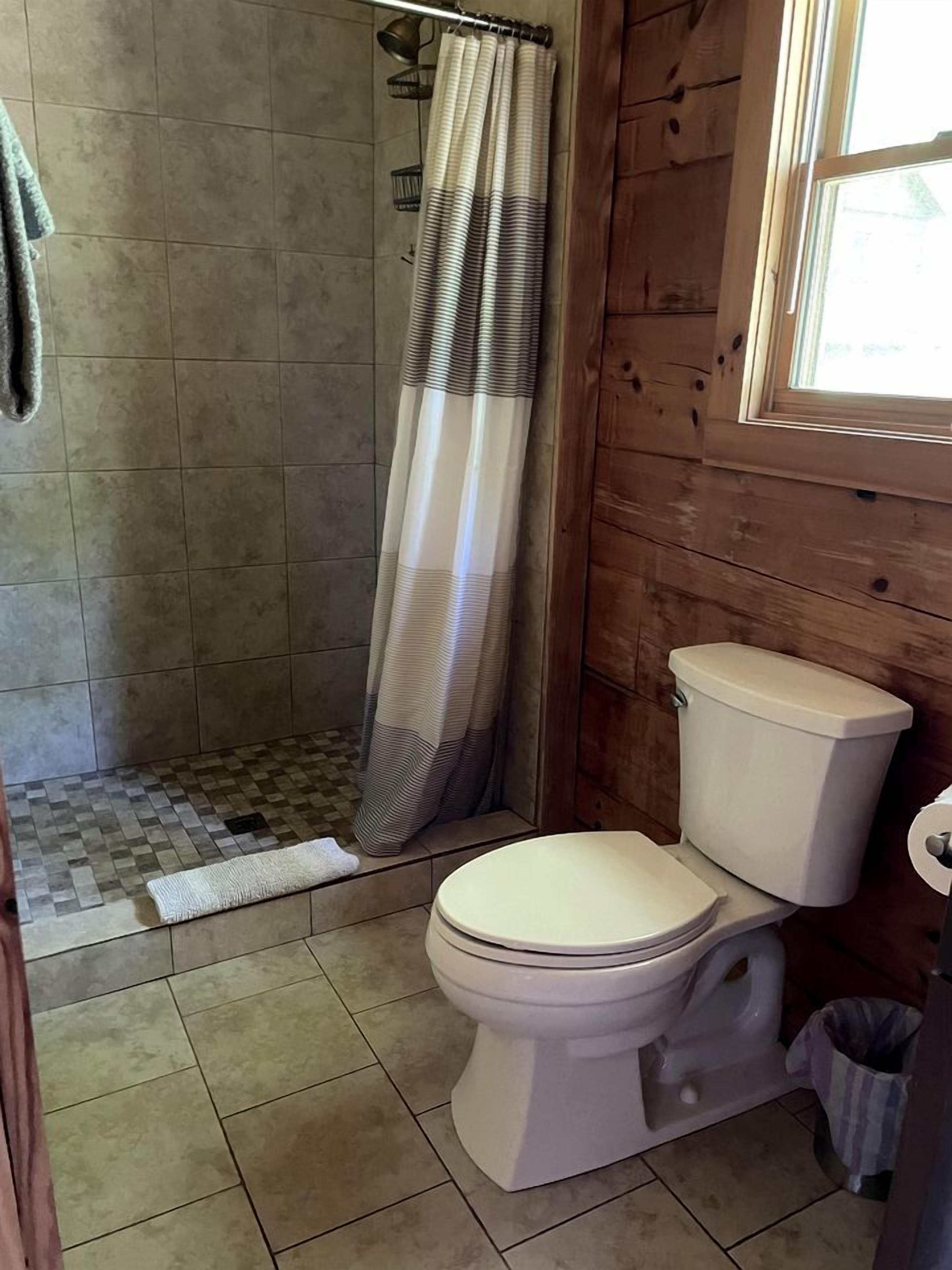 A bathroom with a shower, toilet, and a window.
