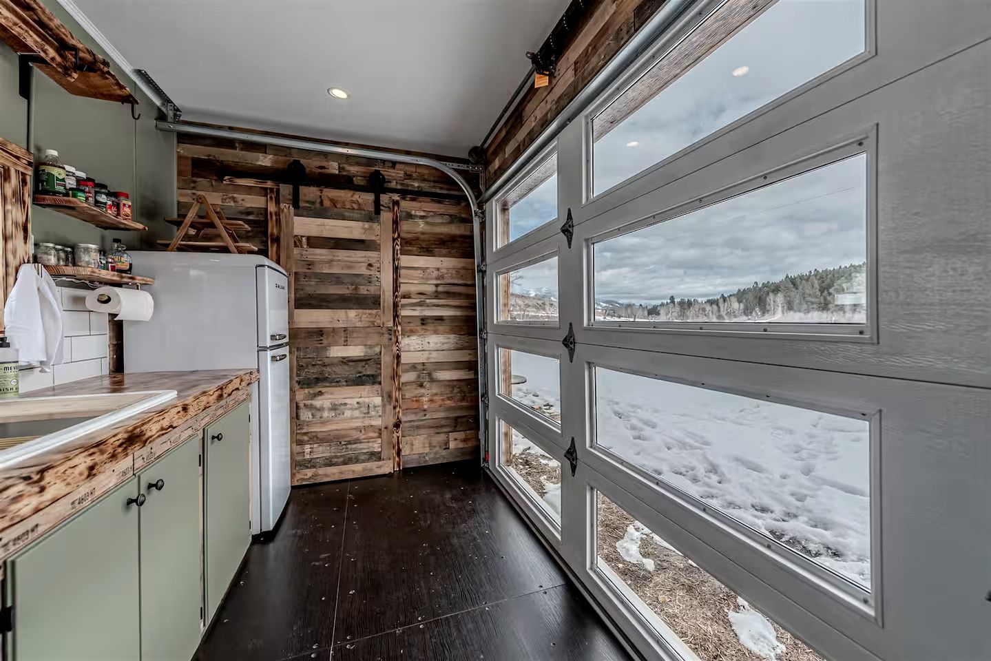 A kitchen with a wooden accent wall, a white refrigerator, and a window with a snowy view.