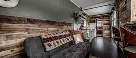 Un espacio de sala acogedor con un sofá, paneles de madera en la pared y una cocina al fondo.