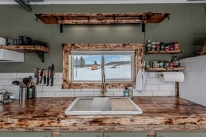 A kitchen with a wooden countertop, a window with a snowy view, and a shelf with kitchen utensils.