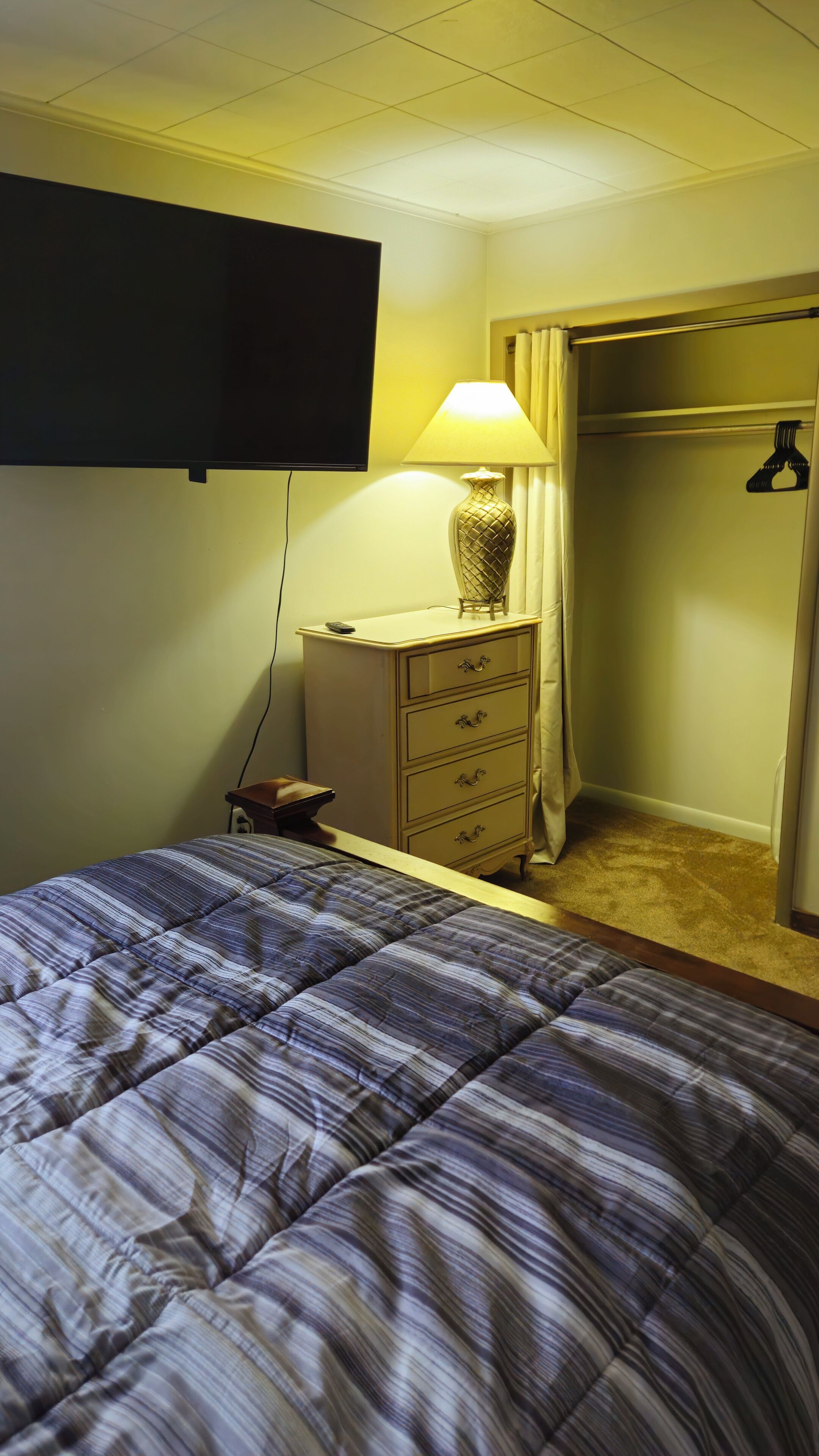 Quarto de hotel com cama, penteadeira, luminária, televisão e armário.
