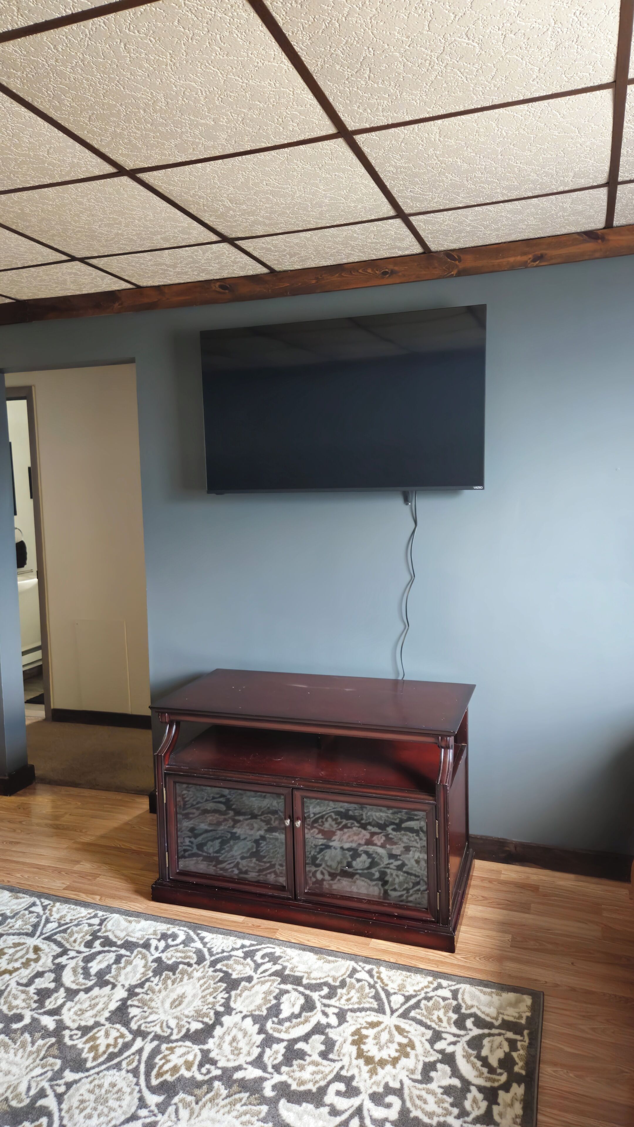 A room with a wooden floor, a patterned rug, a dark wooden cabinet, and a mounted television.