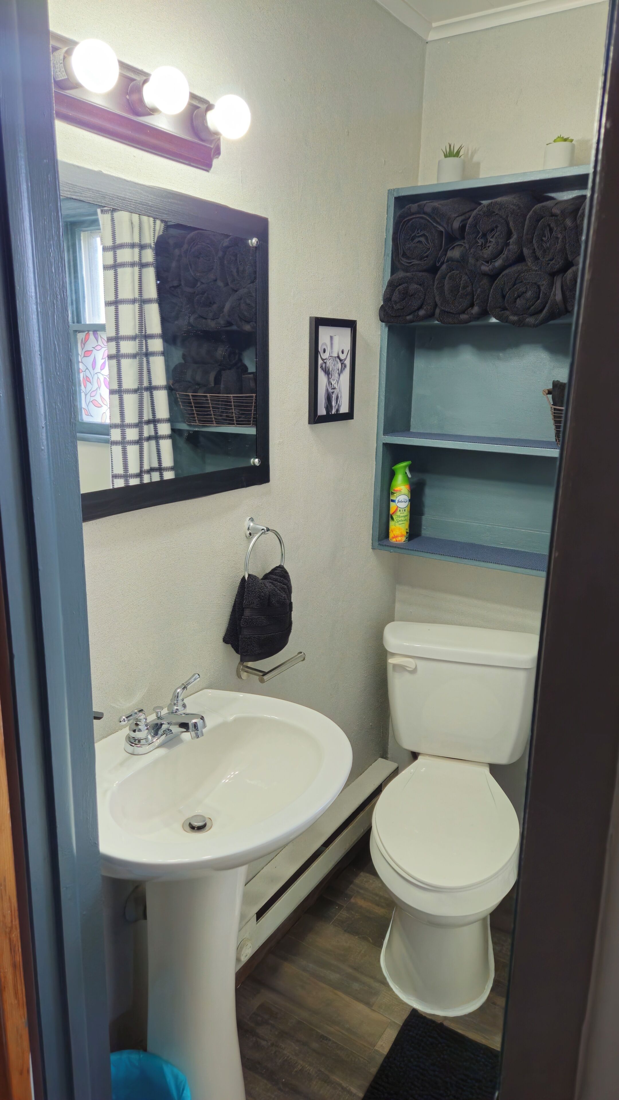 Un bagno con un lavandino bianco, un water, uno specchio e uno scaffale con asciugamani.