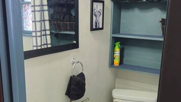 Un bagno con un lavandino bianco, un water, uno specchio e uno scaffale con asciugamani.