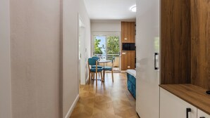 Un couloir mène à une salle à manger avec vue sur l’extérieur, un plancher en bois et un téléviseur fixé au mur.