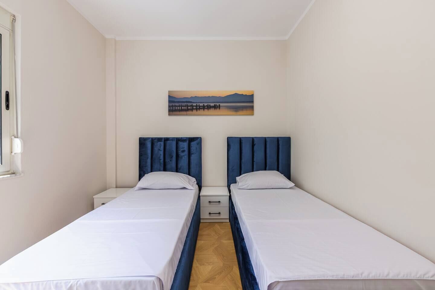 A twin room with two single beds, a small bedside table, a nightstand, and a painting on the wall.