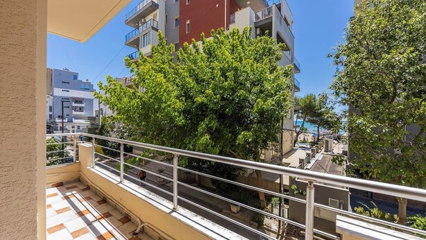 Un balcon doté d’une rambarde en métal, d’un sol carrelé et offrant une vue sur un arbre et des bâtiments.