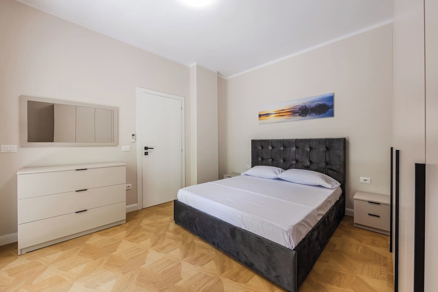 A bedroom with a bed, a dresser, a door, and a painting on the wall.