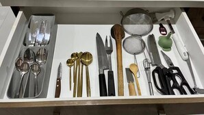 Eine Schublade mit verschiedenen Küchenutensilien, darunter Löffel, Messer und ein Sieb.