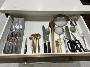 A drawer with various kitchen utensils including spoons, knives, and a strainer.