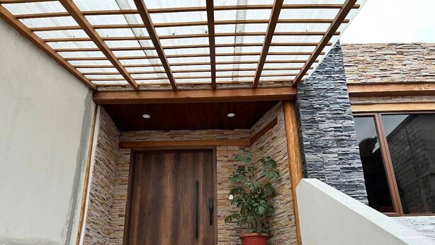 Eine Treppe führt zu einer Holztür, neben ihr eine Steinwand und ein Blumentopf.
