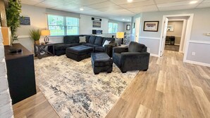 Ein geräumiges Wohnzimmer mit einem Ecksofa, Poufs und einem großen Teppich.