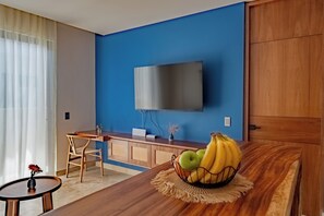 Ein modernes Zimmer mit blauer Akzentwand, einem flachbildfernseher über einem Holzbüro, einem Esstisch mit Obstschale und einem Holzschrank.