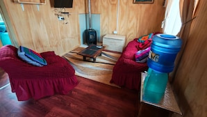 Une pièce chaleureuse avec un décor intérieur en bois, un canapé, une table basse, un distributeur d’eau bleu et un téléviseur fixé au mur.