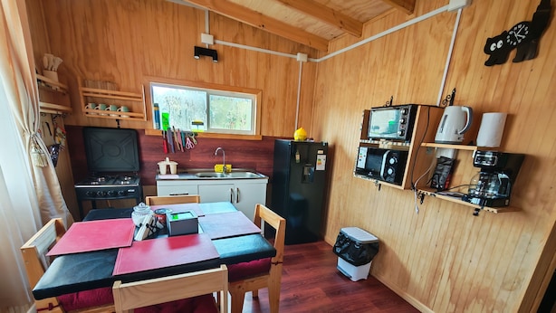 Une cuisine compacte équipée d’une cuisini ère, d’un évier, d’un réfrigérateur et d’un four à micro-ondes. On y trouve une table à manger avec des chaises et une petite poubelle.