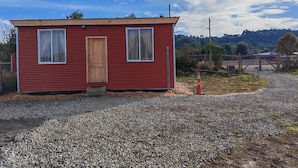 Un petit bâtiment rouge avec une porte en bois et deux fenêtres, entouré de gravier et d’une clôture.