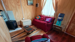 Une pièce confortable avec un canapé rouge, une petite table en bois, un distributeur d’eau et un radiateur.