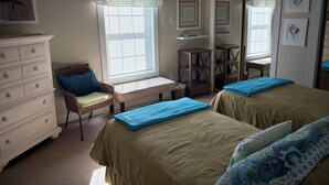 Ein Schlafzimmer mit zwei Betten, einem Schminktisch, einem Stuhl, einer Bank und einem Fenster mit Jalousien.