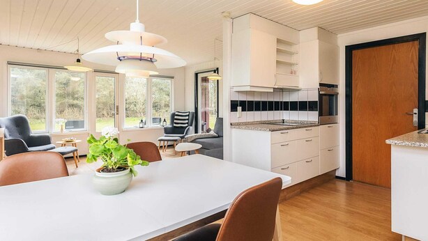 A modern kitchen with white cabinets, a built-in oven, and a dining area with a table and chairs. - 6 Person Holiday Home in Lokken (Lokken)