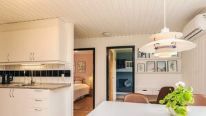 A modern kitchen with white cabinets, a dining area with a white table and brown chairs, and a hanging light fixture. - 6 Person Holiday Home in Lokken (Lokken)