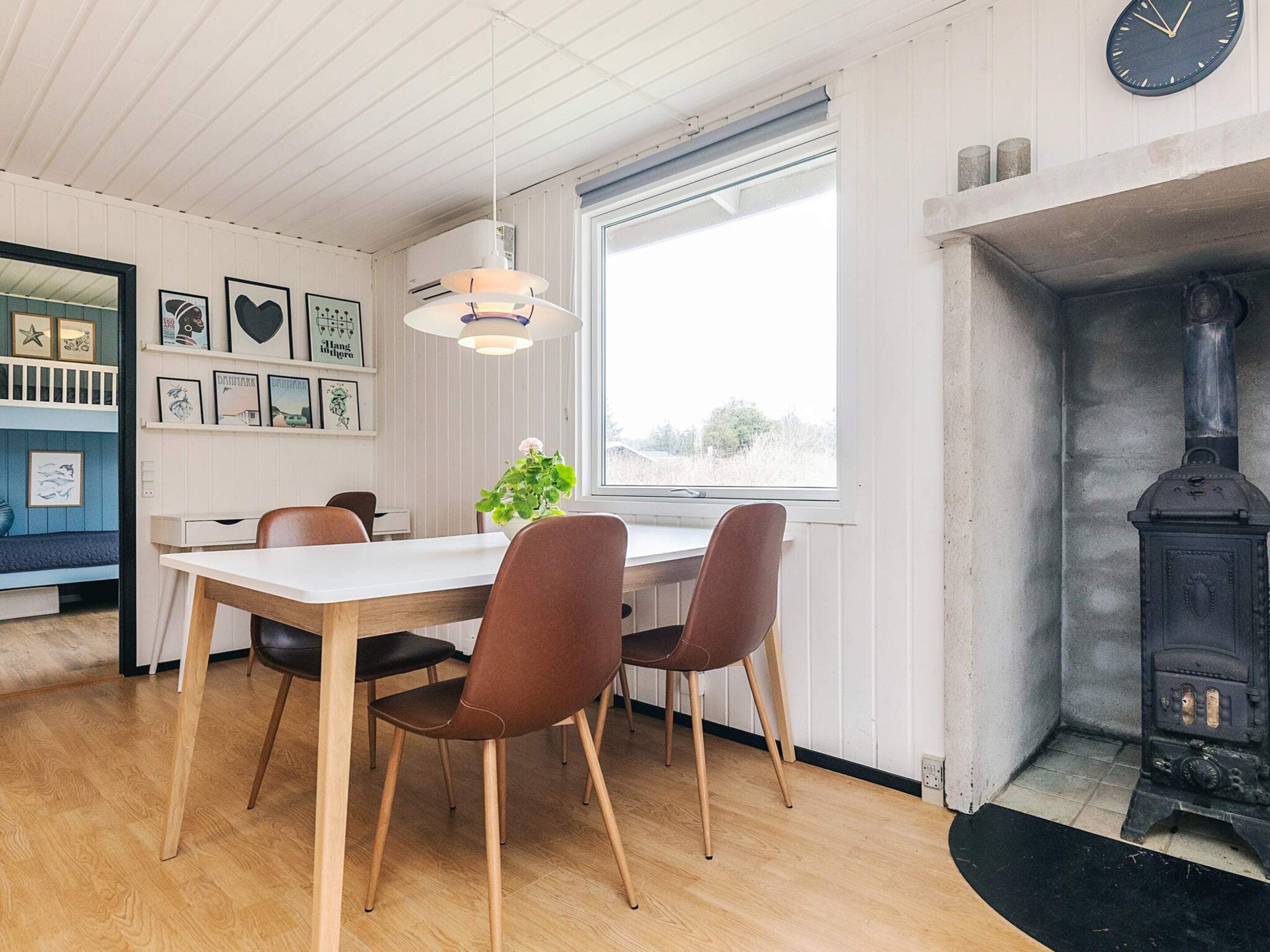 A dining area with a wooden table and chairs, a hanging light fixture, and a view of the outdoors through a window.