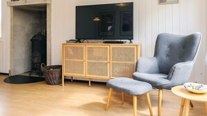 A living room with a television, a blue armchair, a wooden cabinet, and a small round table. - 6 Person Holiday Home in Lokken (Lokken)