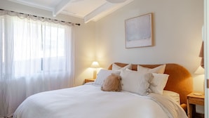 Un lit bien fait, avec des oreillers, une lampe de chevet et un tableau encadré accroché au mur.